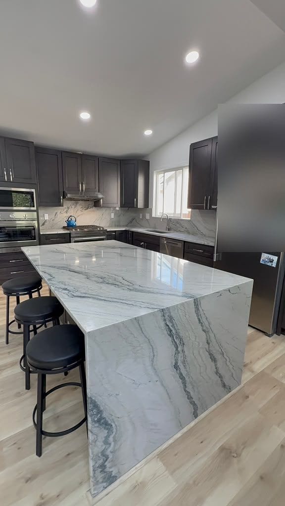 Waterfall island and full-height quartzite backsplash in a dark-cabinet kitchen