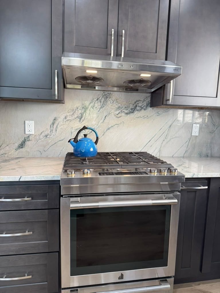 Quartzite slab backsplash behind a gas range with dark shaker cabinets